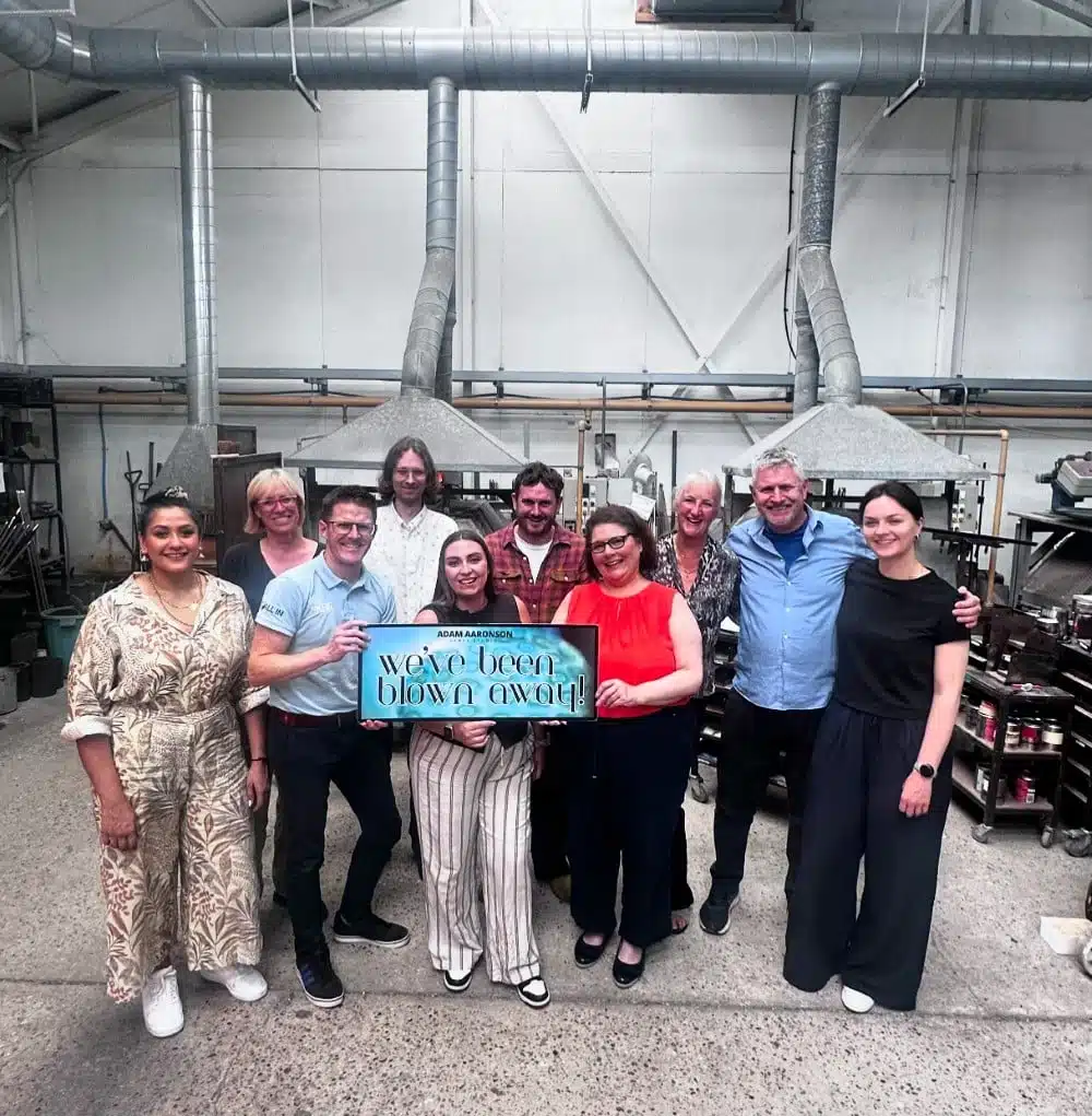 A group of people smiling and holding a sign that says "we've been blown away!" in a workshop.