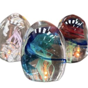 Three glass paperweights with jellyfish designs and internal lights on a white background.