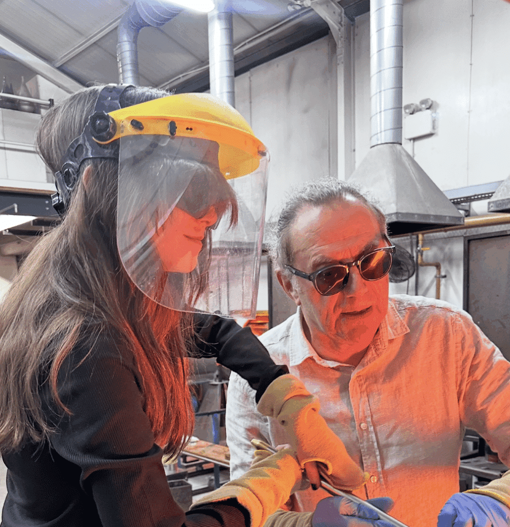 Two people wearing safety gear work together in an industrial studio or workshop.
